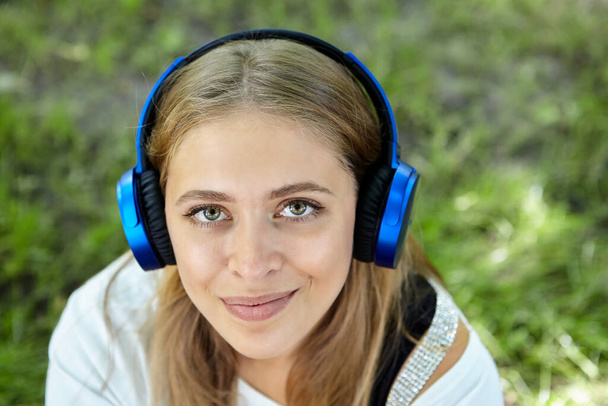 Portrait of beautiful young caucasian cheerful and friendly woman about 25 years old with long blond hair and earphones in public park. Attractive white girl is smiling. - Fotó, kép