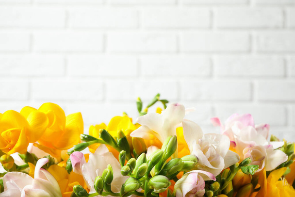 Beautiful blooming freesias against white brick wall. Space for text - Fotoğraf, Görsel
