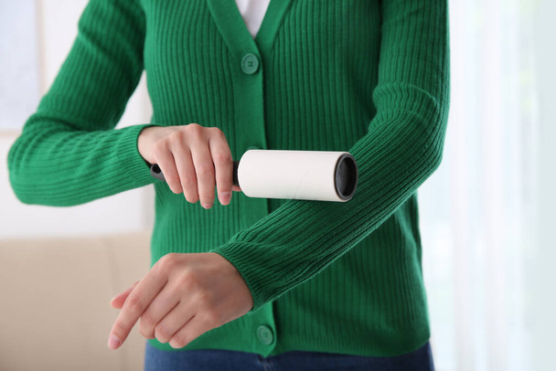 Woman cleaning green jacket with lint roller indoors, closeup - Foto, Imagen