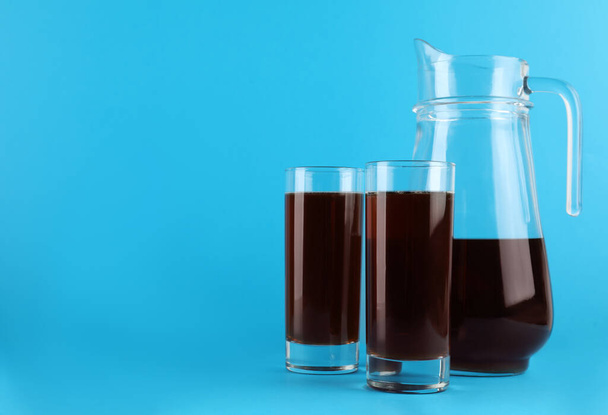 Delicious homemade kvass in glasses and jug on light blue background. Space for text - Fotó, kép