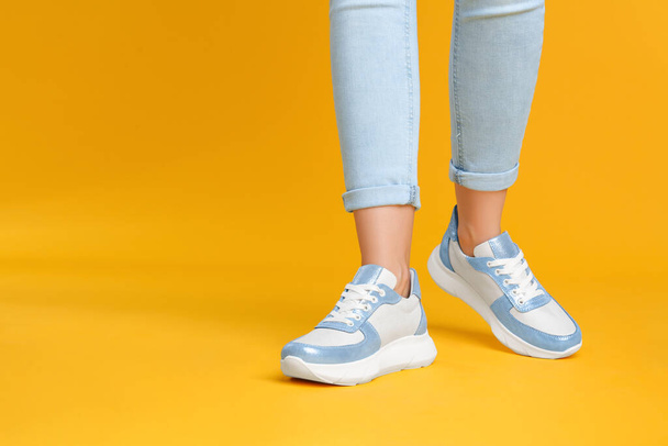 Woman wearing stylish sneakers on yellow background, closeup. Space for text - 写真・画像