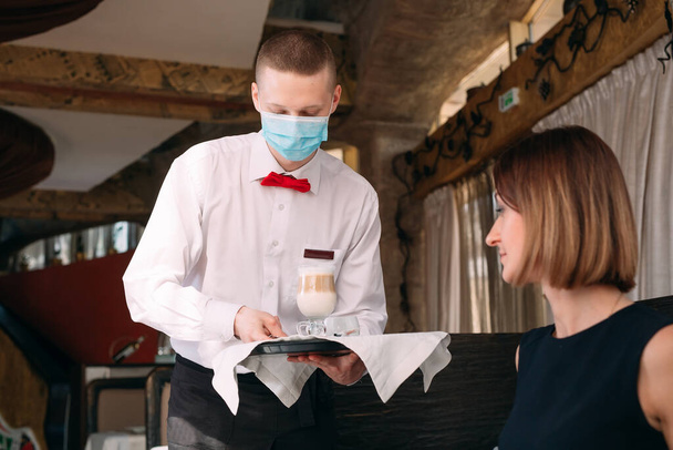 A European-looking waiter in a medical mask serves Latte coffee. - Valokuva, kuva