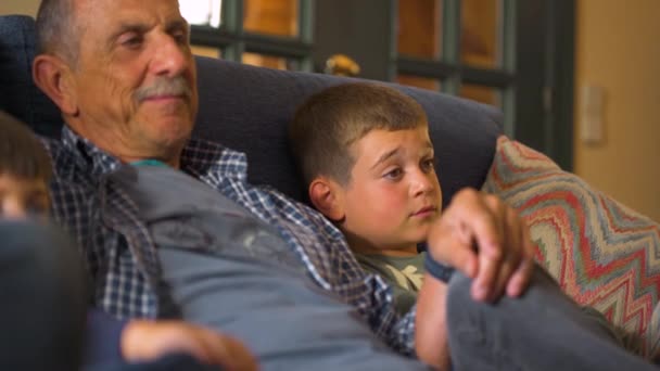 Close-up middelbare leeftijd Kaukasische opa zit op de bank televisie te kijken met zijn twee kleinzonen aan weerszijden. Gelukkige familie momenten. - Video