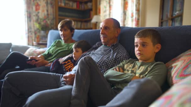 Grandparents and grandchildren sitting on the living room sofa watching television. Home moments in cozy, rustic and old-fashioned house. Medium shot. - Footage, Video