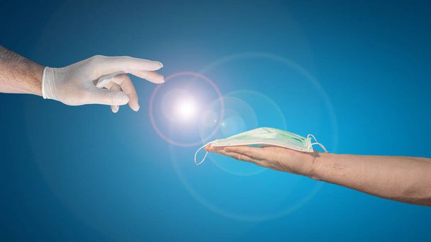 Futuristic banner with a hand in medical glove trying to take a surgical mask from another hand, design concept with copy space for text at gradient blue background and lens flare - Photo, Image