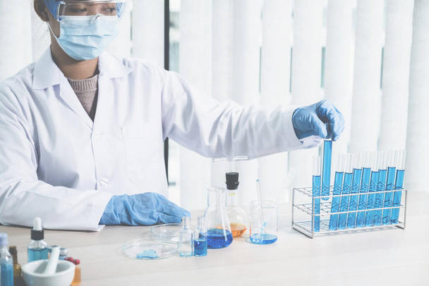 Οι επιστήμονες κρατούν ένα γυάλινο σωλήνα γεμάτο με μπλε χημικό υγρό για έρευνα και ανάλυση σε ένα εργαστήριο. - Φωτογραφία, εικόνα
