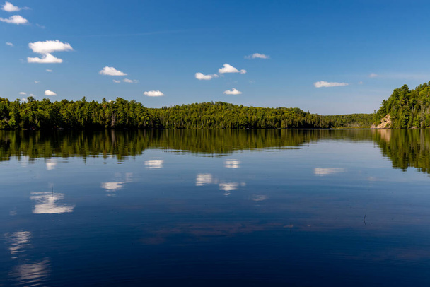 Serene Canadian lake landscape with white cloud reflections and blue sky - Photo, Image