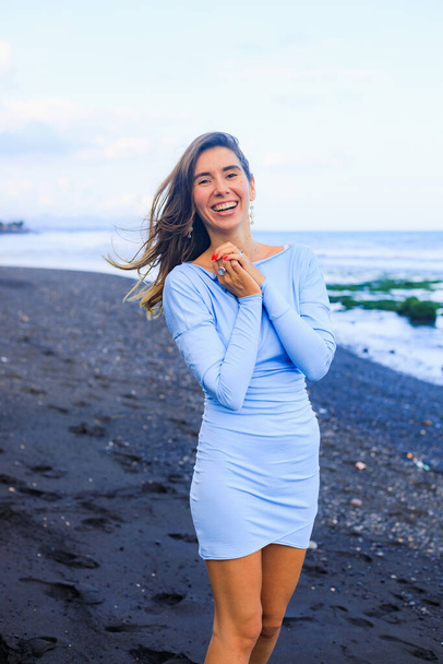 Прекрасна молода жінка, що йде на пляжі з чорного піску. Кавказька жінка у блакитній міні-сукні. Романтична концепція. Подорожуючий спосіб життя. Балі (Індонезія) - Фото, зображення