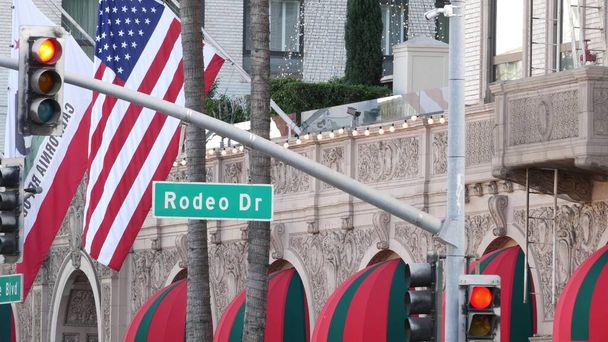 World famous Rodeo Drive Street Road Sign in Beverly Hills κατά αμερικανική σημαία Ηνωμένες Πολιτείες. Λος Άντζελες, Καλιφόρνια, ΗΠΑ. Πλούσια πλούσια ζωή καταναλωτισμός, μάρκες πολυτελείας, υψηλής ποιότητας κατάστημα έννοια - Φωτογραφία, εικόνα