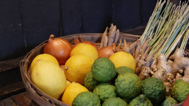 Mand met groenten en fruit. Gevlochten mand met diverse citrusvruchten en groenten geplaatst op de vloer in de buurt van houten muur. - Foto, afbeelding