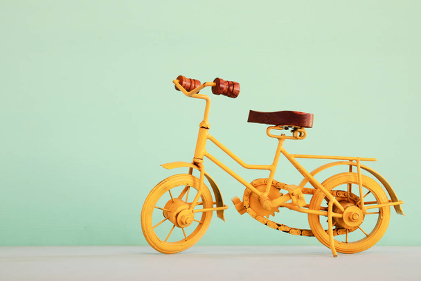 Vintage metal yellow bicycle toy over wooden table and pastel background - Foto, imagen