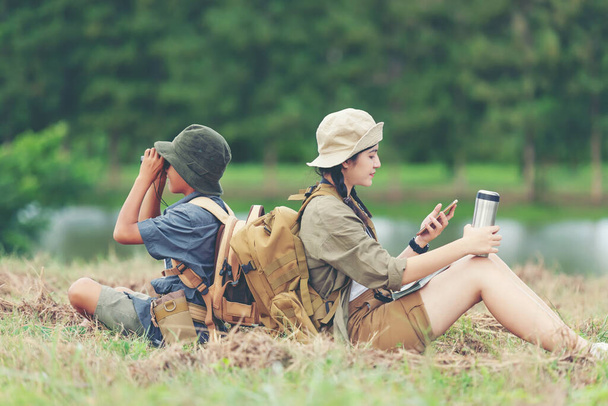 Asia young woman and boy travel nature summer trips. Asia people tourism sitting on nature park check in and holding  binoculars, happy fun explore adventure camping outdoors for leisure and destination. Travel Lifestyle Concept - Fotoğraf, Görsel