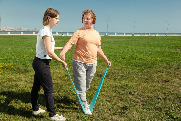 Mujer joven entrenador ayuda a la mujer mayor haciendo ejercicios de estiramiento. - Foto, imagen