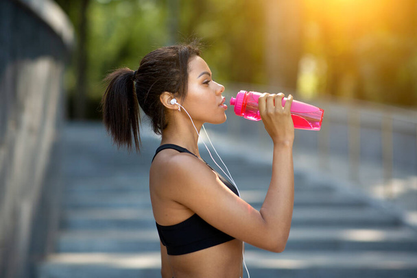 Closeup of fitness model drinking water during training at park - Photo, Image