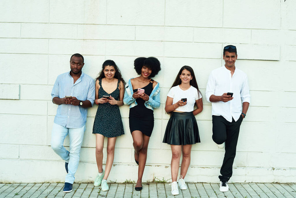 Gruppe von Freunden, die über etwas lachen, das sie auf ihr Smartphone schauen. Junge Menschen sind süchtig nach neuen Technologietrends. Jugend-, Technologie-, Sozial- und Freundschaftskonzept. - Foto, Bild