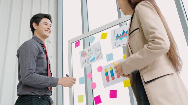 Business people work on project planning board in office and having conversation with coworker friend to analyze project development . They use sticky notes posted on glass wall to make it organized . - 写真・画像