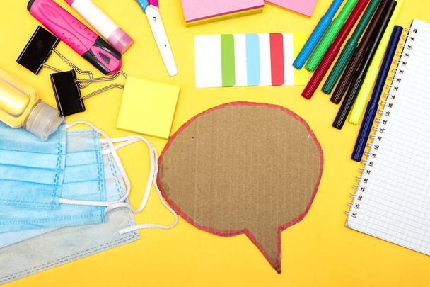Back to school, school supplies with medical face mask and empty notebook and chat bubble on a yellow background. Protection of schoolchildren and students from the virus - Photo, Image