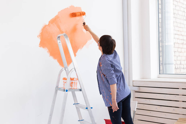 Mujer de mediana edad pintando las paredes de un nuevo hogar. Concepto de renovación, reparación y redecoración. - Foto, imagen