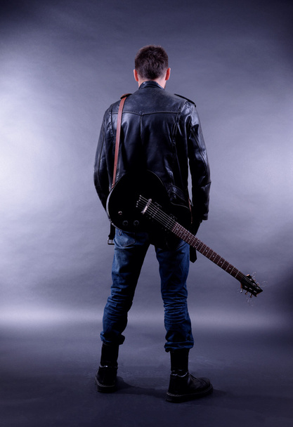 Young musician with guitar on dark color background - Foto, Bild