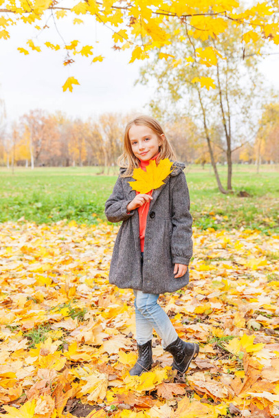 Happy young girl playing with falling yellow leaves in beautiful autumn park on nature walks outdoors. Little child holding autumn orange maple leaf - Valokuva, kuva