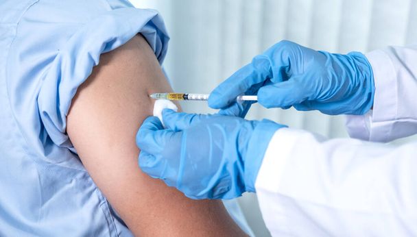 Die Hand des Arztes hielt eine Spritze und wollte gerade einen Patienten in der Klinik impfen, um die Ausbreitung des Virus zu verhindern. - Foto, Bild