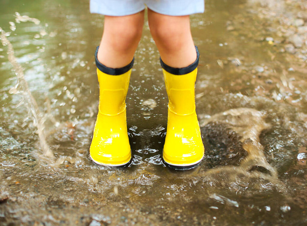 Маленькая девочка в жёлтых сапогах и пальто, прыгающая в дождливый день - Фото, изображение