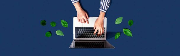 Person using a laptop computer with green leaves - Foto, afbeelding