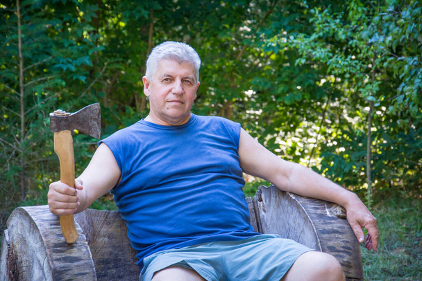 Im Sommer sitzt ein Mann in der Natur auf einem Baumstamm mit einer Axt. - Foto, Bild