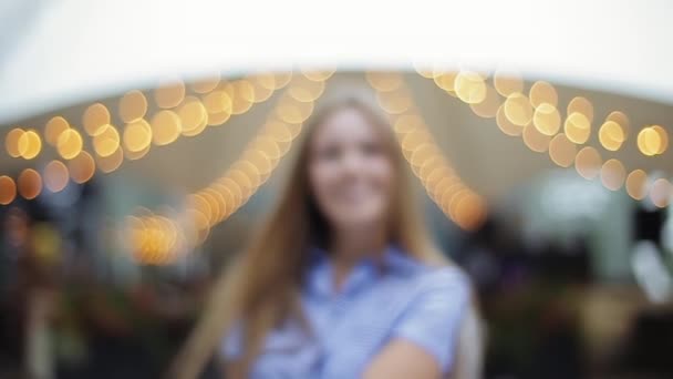 Close-up front view of cute happy pleasant girl in striped dress approaching camera out of focus laughing on blurred background of street lights in slow motion. Portrait of positive woman in evening - Footage, Video