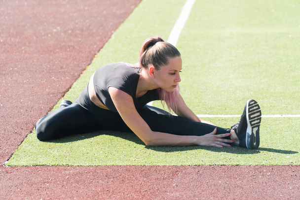 The young athlete is engaged in a warmup before fitness training. Stretching the joints of the legs in running stadium - Fotografie, Obrázek