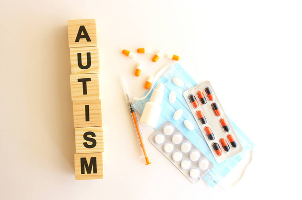 The words AUTISM is made of wooden cubes on a white background with medical drugs and medical mask. Medical concept. - Fotoğraf, Görsel