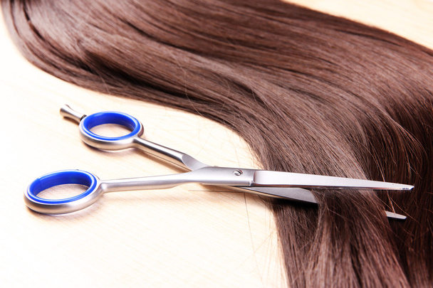 Long brown hair and scissors on wooden background - Foto, Imagen
