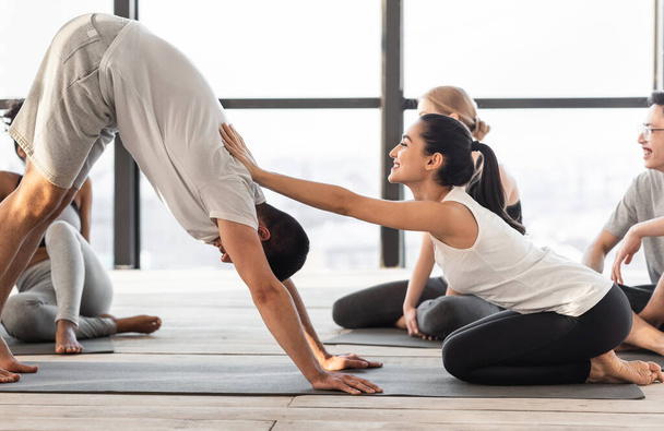 Entraîneur féminin corrigeant yoga débutant à la formation en classe de groupe en studio - Photo, image
