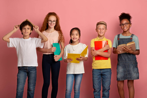 Multinational group of kids with books and notebooks ready for school on pink studio background - Fotoğraf, Görsel
