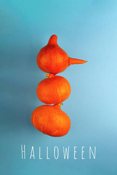 Een sneeuwpop met een wortelneus van drie oranje pompoenen op een blauwe achtergrond. Halloween concept. - Foto, afbeelding