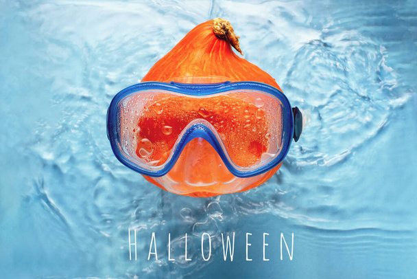 Orange pumpkin swimmer in a mask in blue water. Halloween concept. - Photo, Image