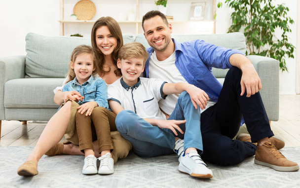 Parents And Two Kids Sitting Near Sofa In Living Room - Photo, Image