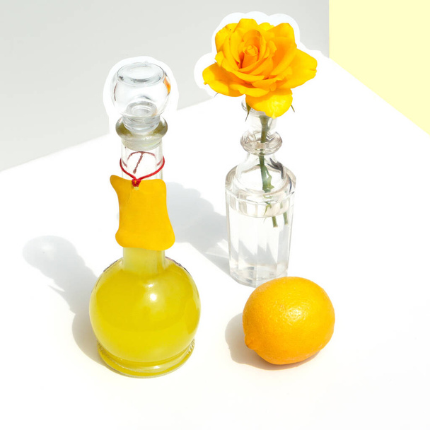 Μπουκάλι ιταλικό limoncello, λεμόνι και κίτρινο τριαντάφυλλο. Σύγχρονη μινιμαλιστική νεκρή φύση σε γεωμετρικό φόντο με ήλιο και σκιές. - Φωτογραφία, εικόνα