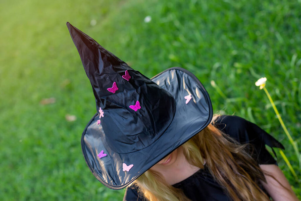 Cadıların cadılar bayramı kostümlü uzun saçlı, yeşil çimenlerde oturan Kafkasyalı sarışın kız. - Fotoğraf, Görsel