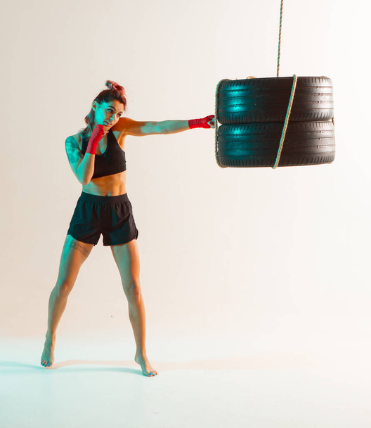 Athletic girl fighter boxing on punching bag in studio in neon light. Mixed martial arts poster - Photo, Image