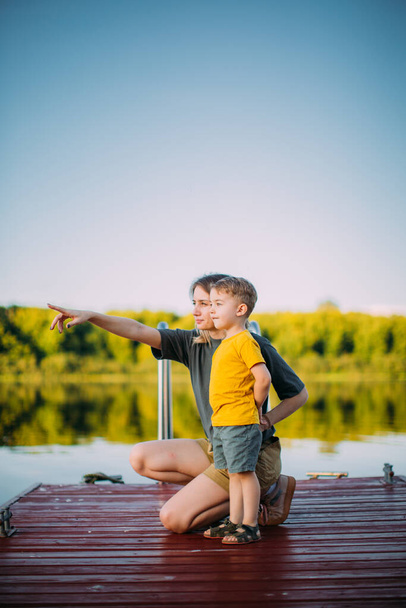 Cool baby boy with mother looking on river standing on pier. Summer photography for blog or ad about family and travel - Valokuva, kuva