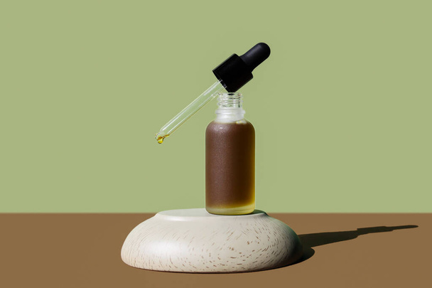 Cosmetic herbal, hemp oil bottle with dropper removed on stone pedestal. Poster, mockup, banner. Brown grassy colors. Frosted vial with moisturizing emulsion, serum. Natural skin hydration, body care - Fotó, kép