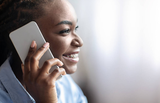 Communication mobile. Gros plan de sourire femme noire parlant sur téléphone portable, vue de côté - Photo, image