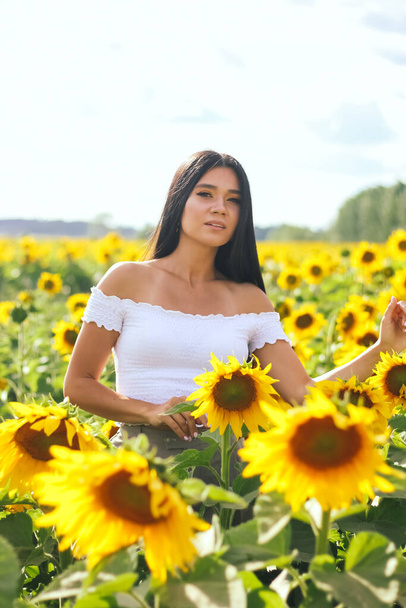 Beautiful brunette woman in a white top on the field with sunflowers. Yellow sunflowers. Close plan. - Photo, Image