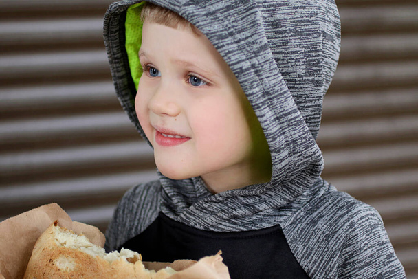 Funny blondheared toddler holding in the arms Georgian bread on the street.Happy smile on his face.Closeup photography of cute boy.Copy space for text. - Photo, Image