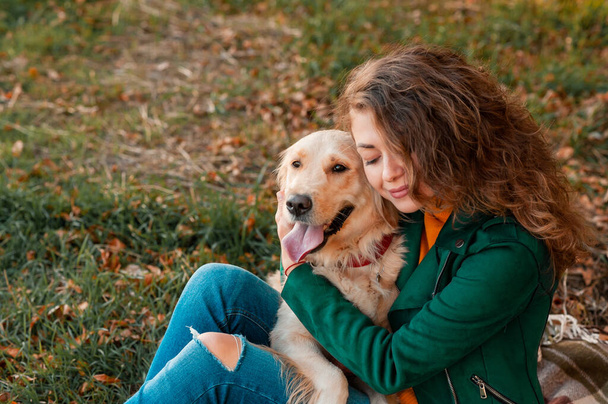Szczęśliwa kobieta odpoczywa ze swoim psem golden retriever. Kobieta cieszy się na świeżym powietrzu ze swoim zwierzakiem. kobieta trenuje na zewnątrz jesienią - Zdjęcie, obraz