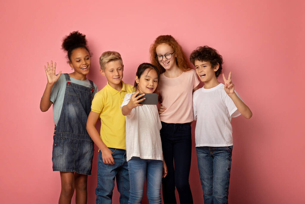Cute diverse schoolchildren taking selfie with cellphone on pink background - Photo, Image