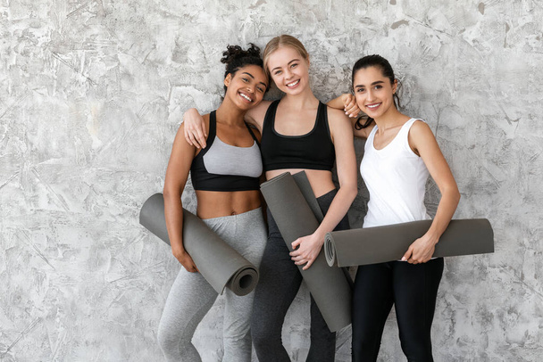 Concepto Fitness y Deporte. Chicas multiétnicas con colchonetas de yoga posando cerca de la pared - Foto, imagen