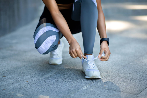 Крупный план черной девушки в спортивной одежде, завязывающей шнурки перед пробежкой - Фото, изображение