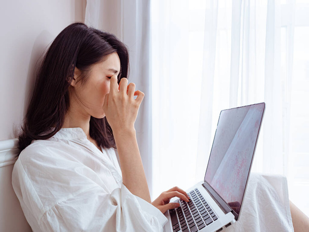 Aziatisch jong vrouw wrijven haar moe ogen bij het gebruik van laptop. - Foto, afbeelding